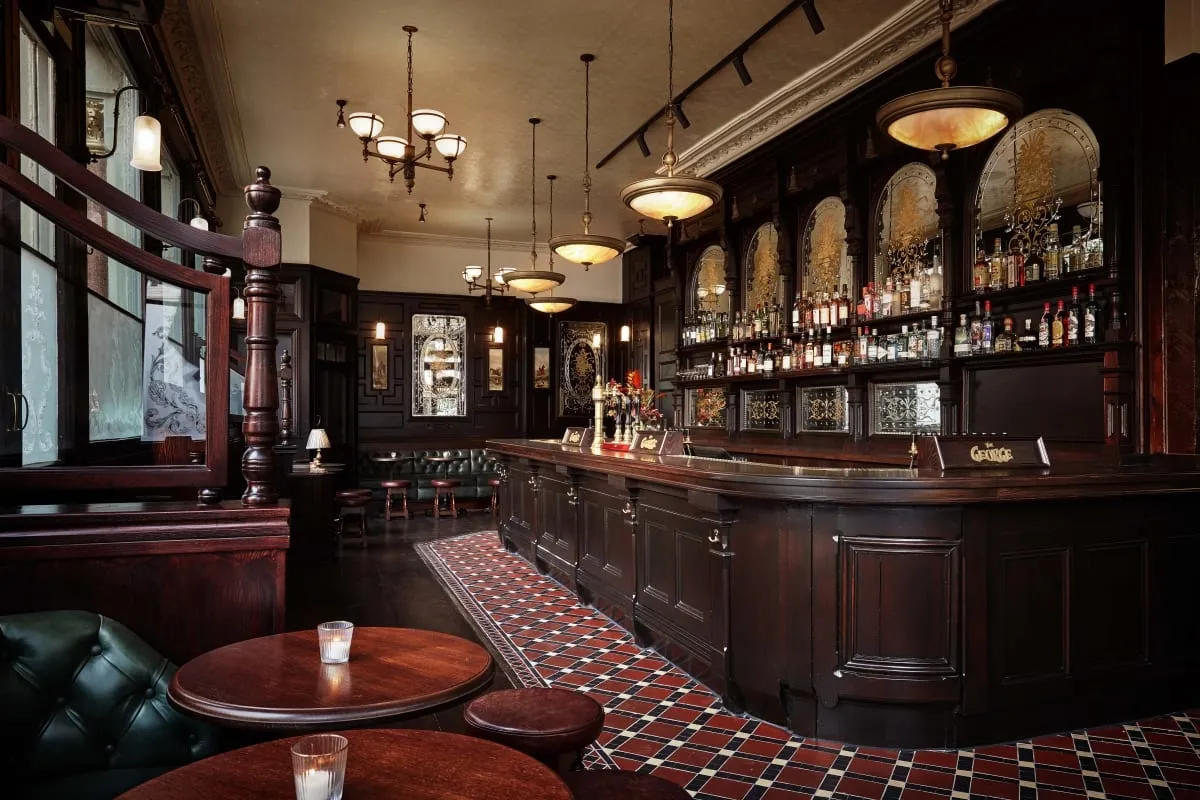A row of arched, etched and gilded mirror bays behind the bar at The George, Fitzrovia, with a diamond-patterned tiled floor in front