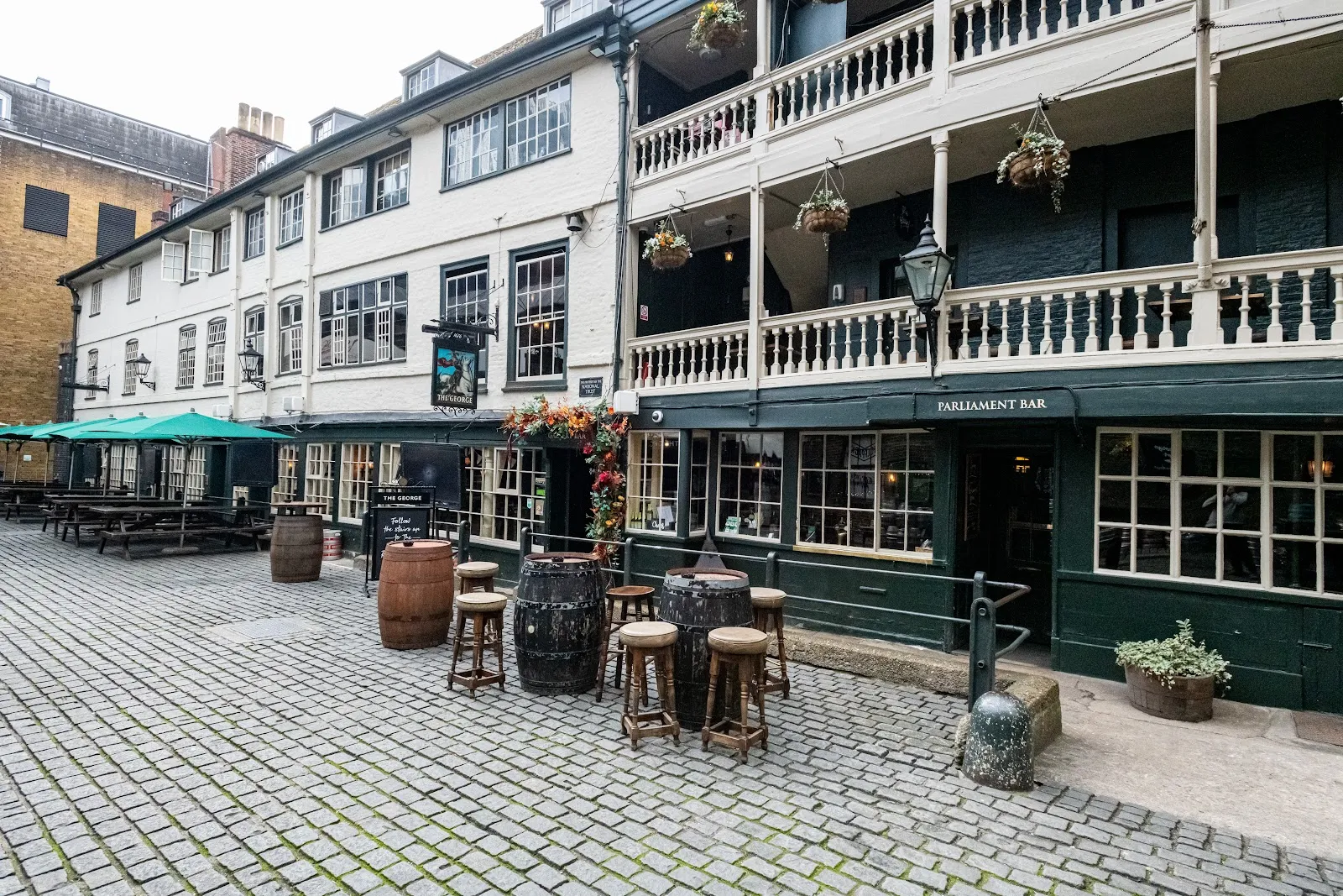 The galleried courtyard of the George Inn in Southwark, with barrels for tables and the Parliament Bar sign