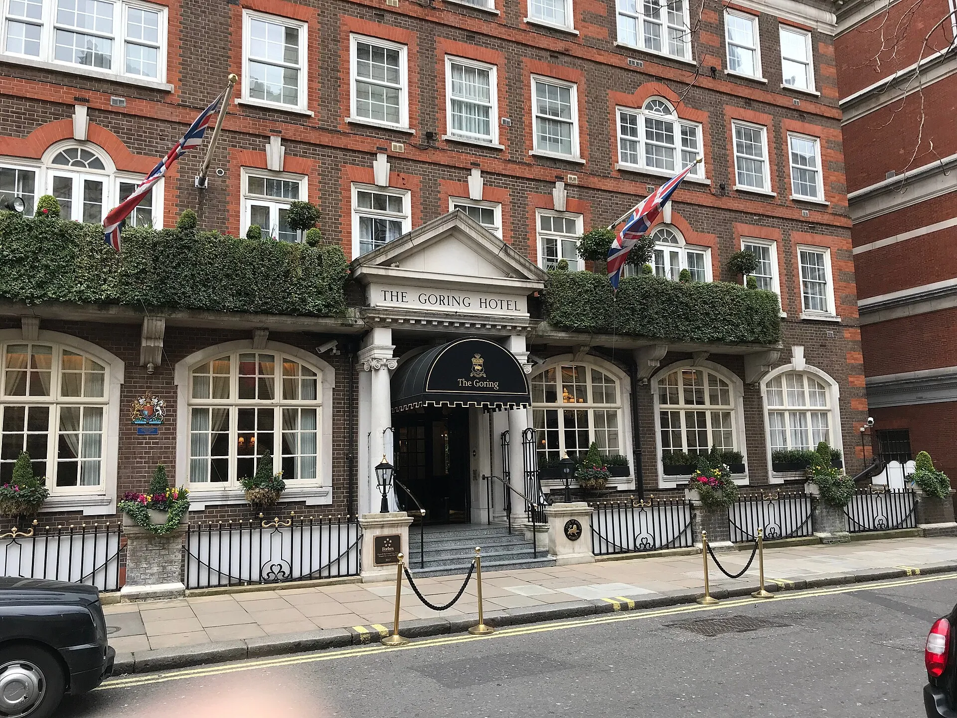 The front of The Goring on Beeston Place: a red-brick building with a white portico reading The Goring Hotel, a black awning over the steps, Union flags and ivy along the first-floor balcony