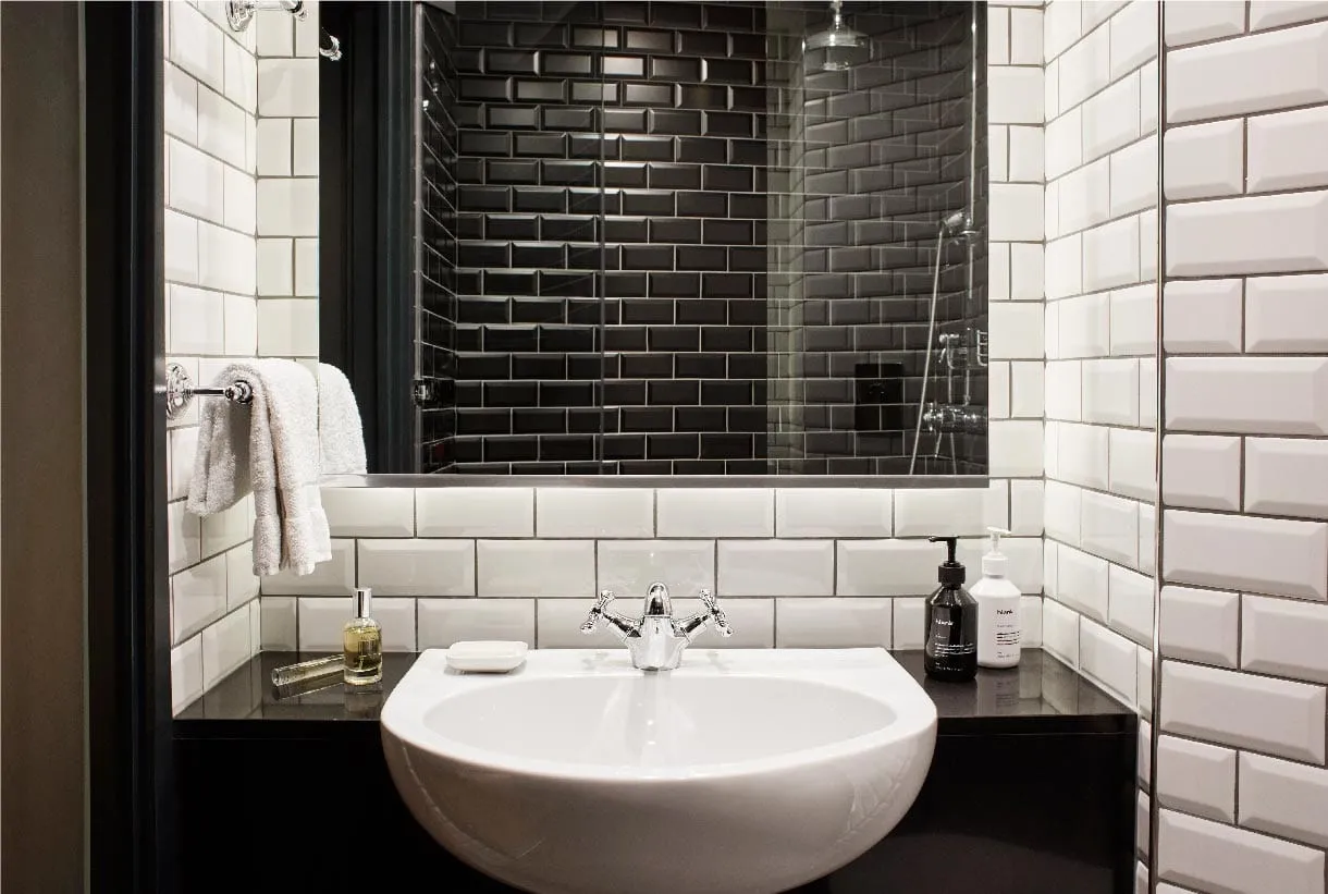 The bathroom of a Hoxton Holborn room, with white and black subway tile and a dark stone vanity