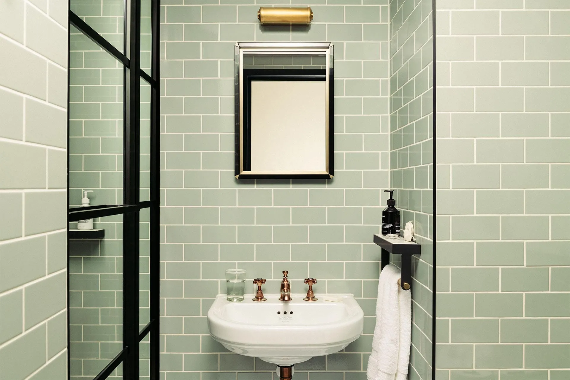The bathroom in a room at The Hoxton, Southwark, tiled in sage green with brass fittings