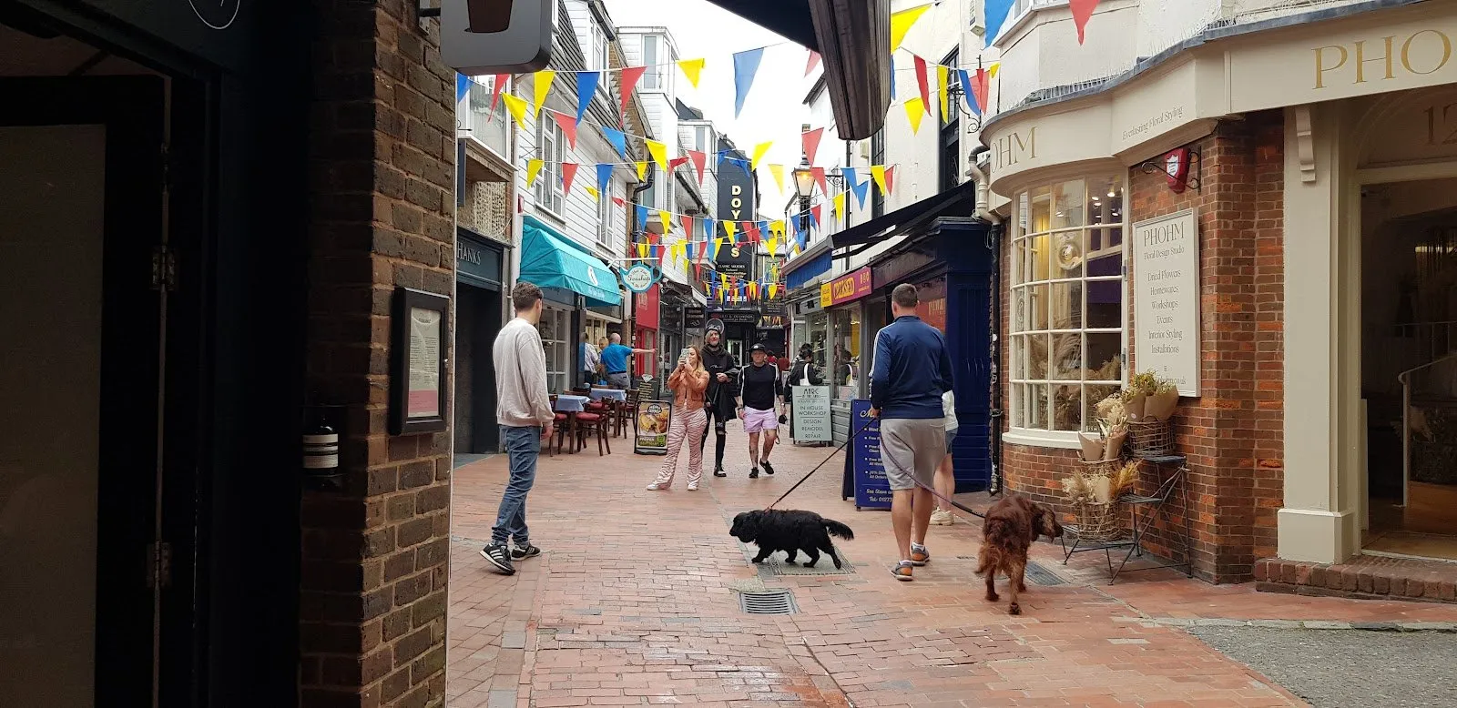 A narrow brick-paved lane in Brighton hung with bunting, lined with independent shopfronts including a florist
