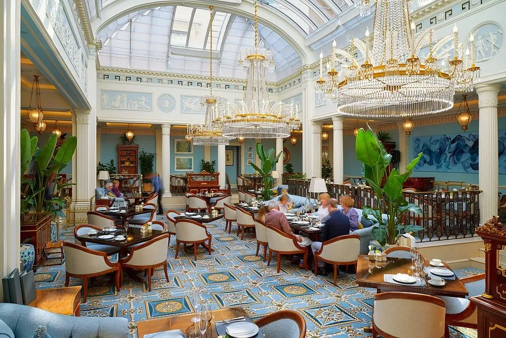 The Céleste dining room under its glass dome, Wedgwood blue and white plasterwork, chandeliers and palms above a blue patterned carpet