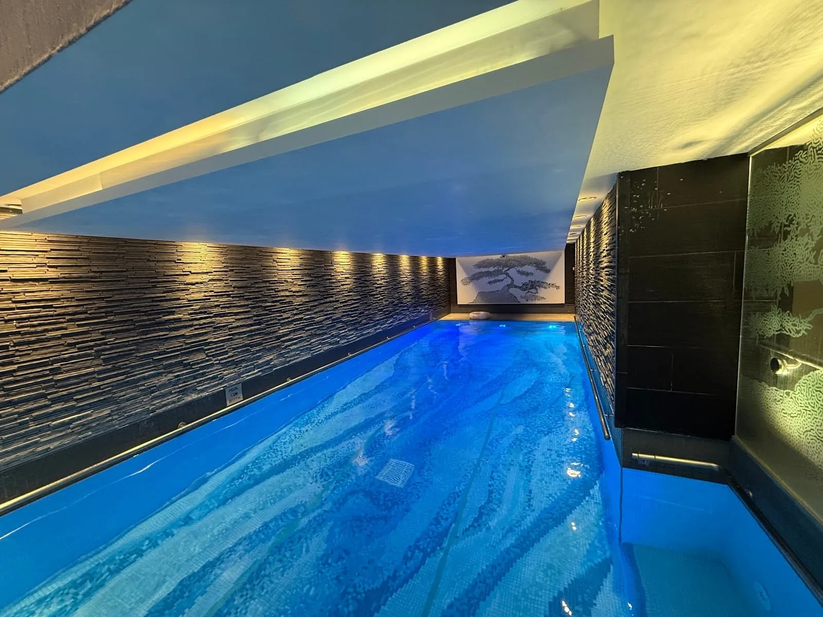 The indoor pool at The Langham, along a slate-clad wall, with a mural at the far end