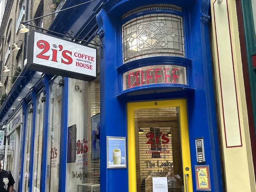 The bright blue frontage of 4 Bull's Head Passage, a 2i's Coffee House sign hanging above and a yellow door whose glass is lettered Two Eyes Speciality Coffee House and The Leaky Cauldron
