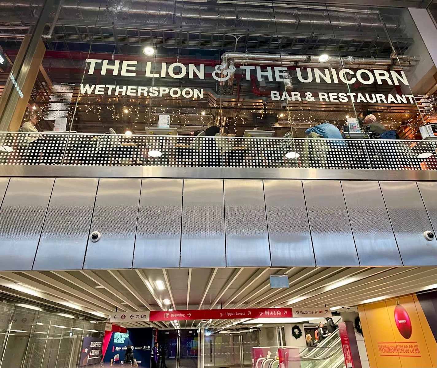 Signage for The Lion, The Unicorn at Waterloo station, seen from the concourse beneath the platforms with exposed ceiling ductwork above