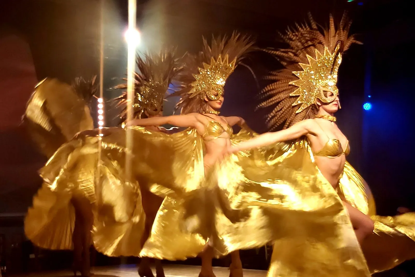 Dancers in gold feathered headdresses and capes performing on stage