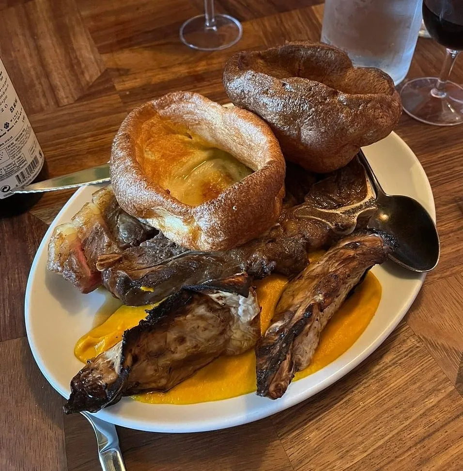 A sharing roast at The Marksman: beef and pork on a bed of carrot puree with charred hispi cabbage, under two large Yorkshire puddings, one filled with cauliflower cheese