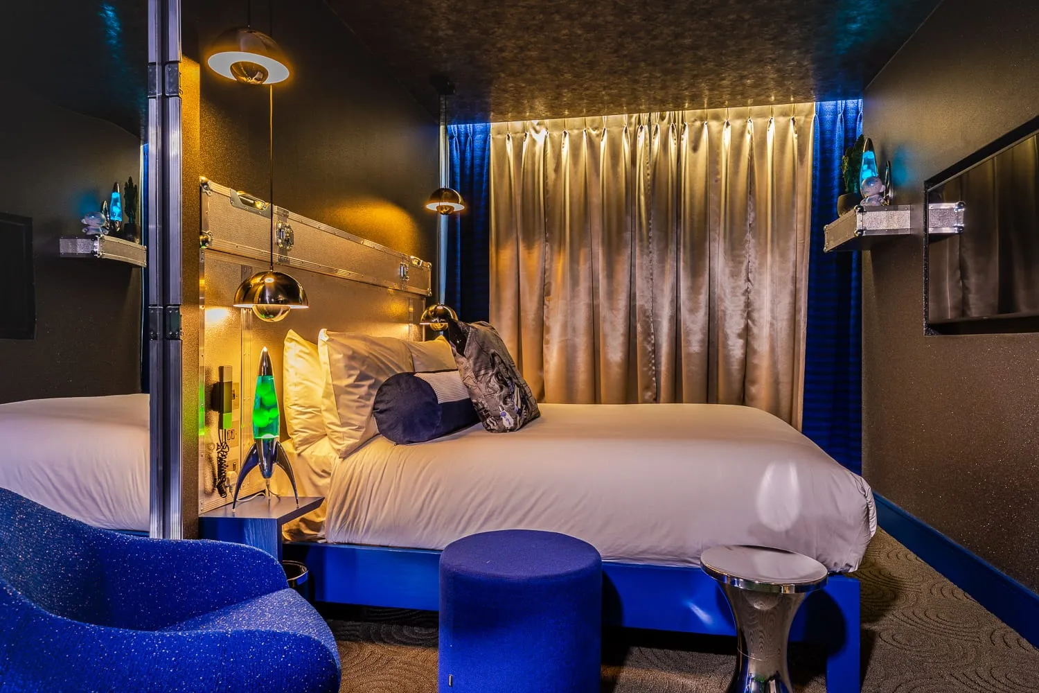 A themed room at the Megaro, with a metallic flight-case style headboard, hanging globe lights and a lava lamp on the nightstand