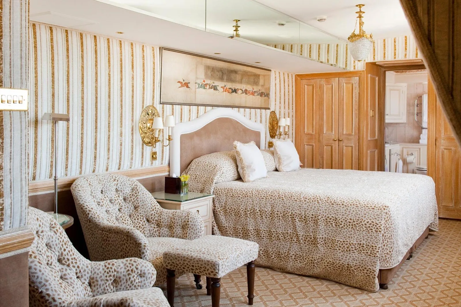 A bedroom at The Milestone Hotel with a leopard-print bedspread and matching armchairs, striped wallpaper and fitted carpet