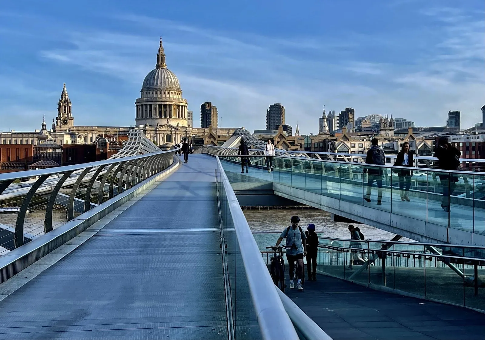The steel deck of the Millennium Bridge running north across the Thames with the dome of St Paul's Cathedral at the far end, a few people crossing