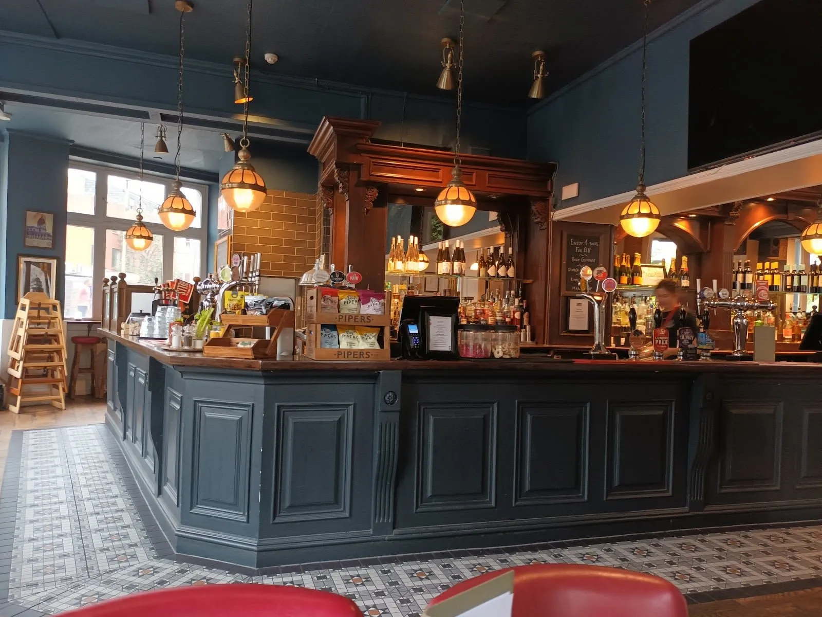 The bar at The Mitre, with a dark panelled counter, hanging globe lamps and a tiled floor