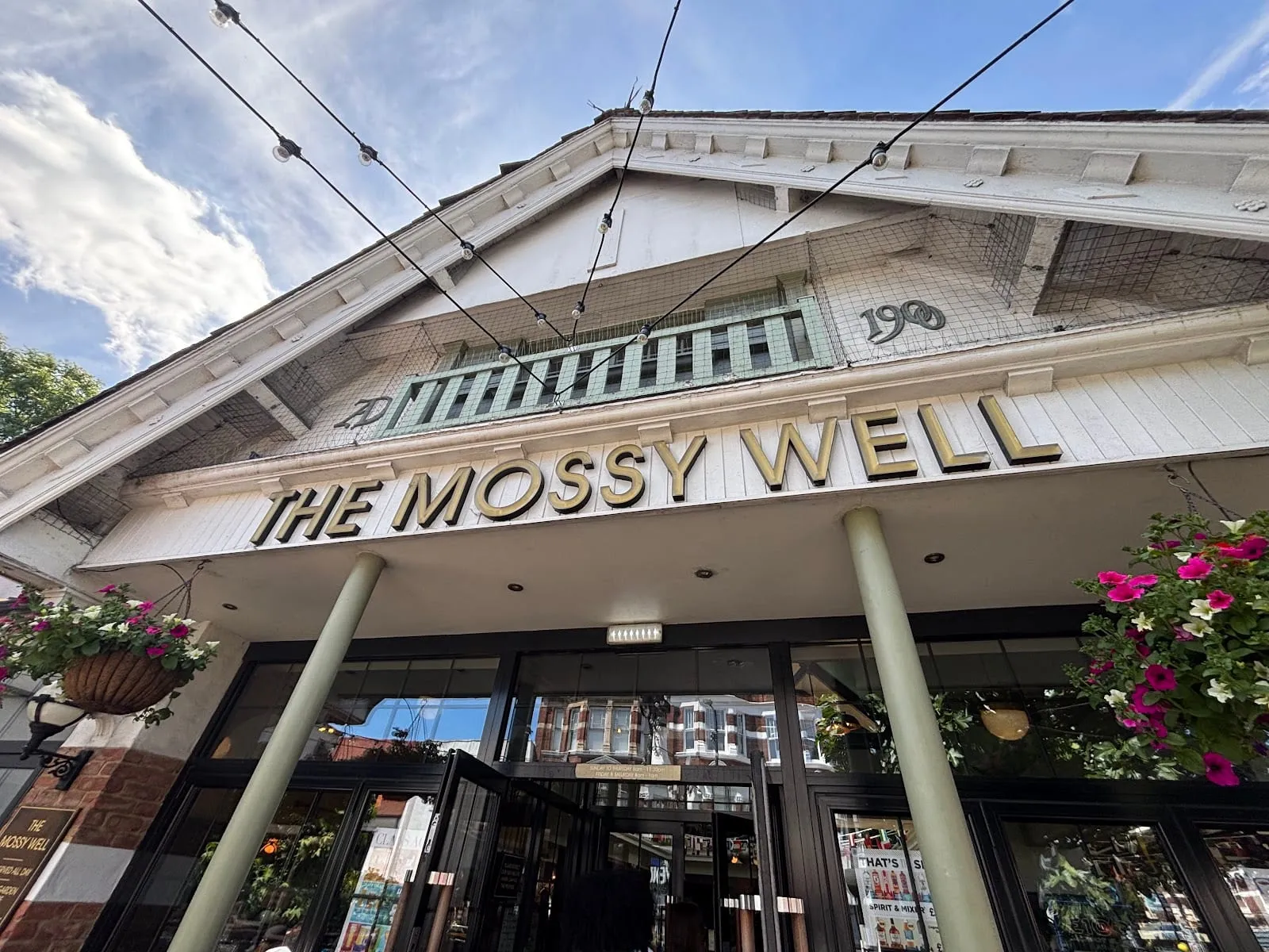The white gabled frontage of The Mossy Well in Muswell Hill, with the date 1900 set into the tilework above the entrance
