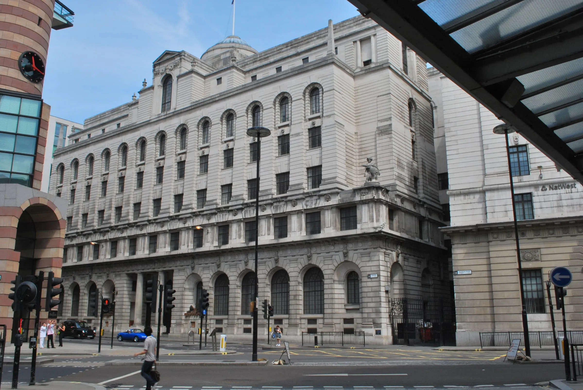 The Portland stone former Midland Bank on Poultry, designed by Edwin Lutyens and now The Ned hotel, seen across the Bank junction with a black cab and pedestrians in front and No 1 Poultry's striped corner on the left
