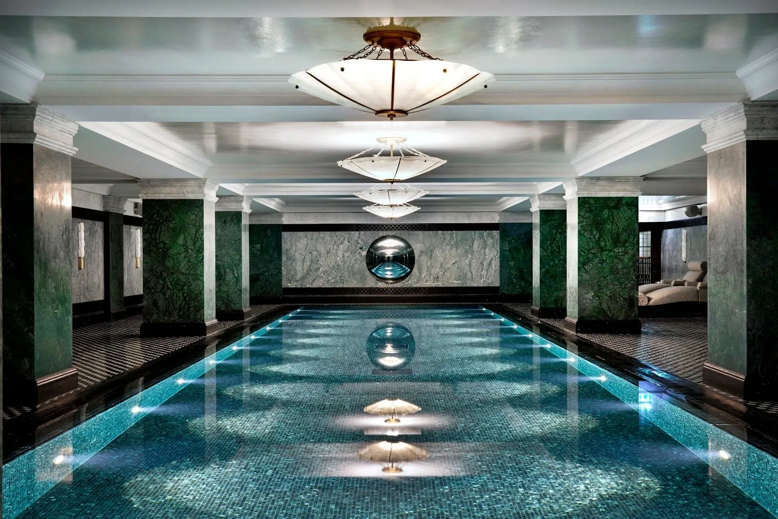 The basement spa pool at The Ned, with green marble columns and a mirrored sphere at the far end