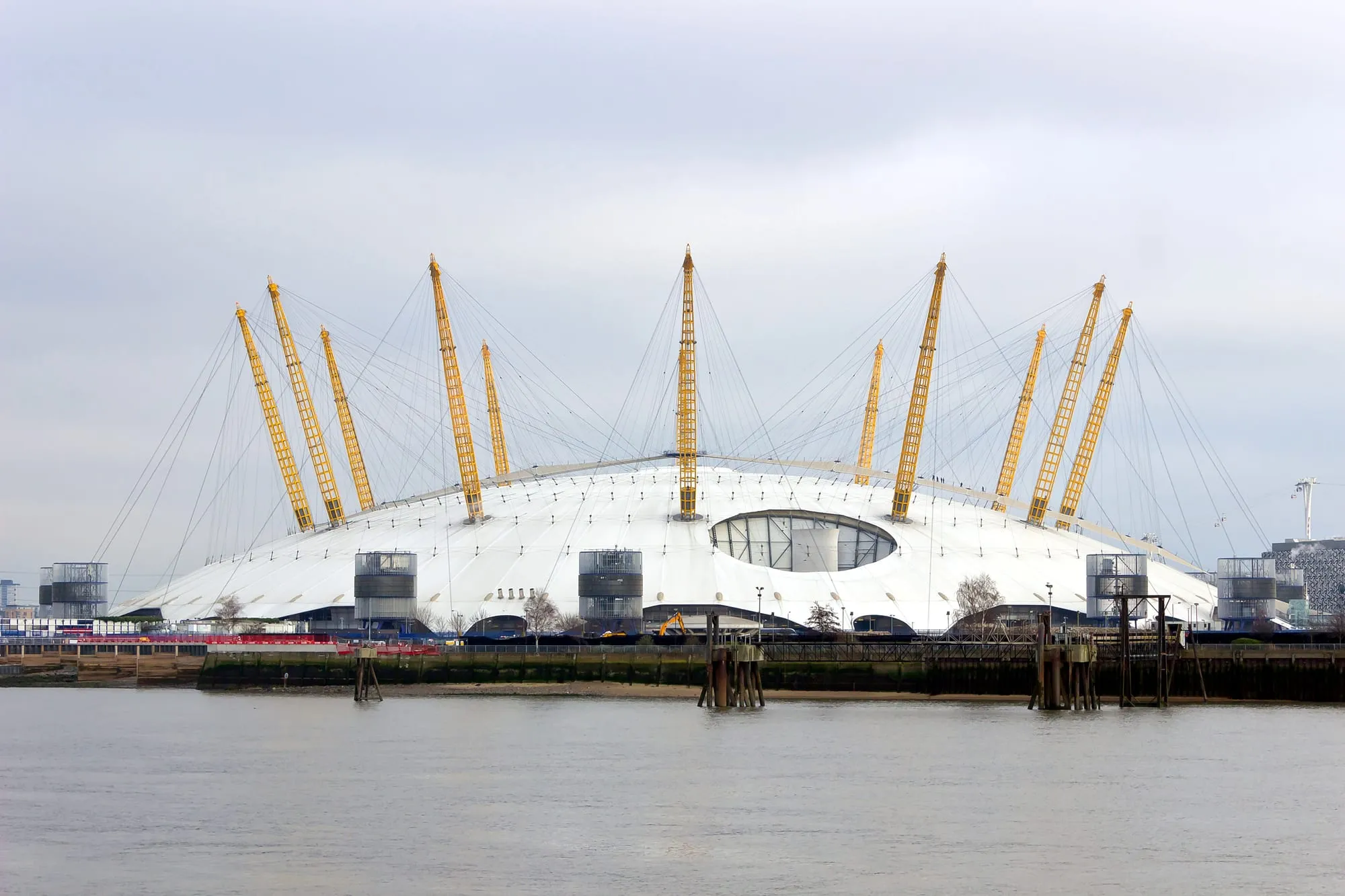 The O2's white dome and yellow masts seen across the Thames under a grey sky