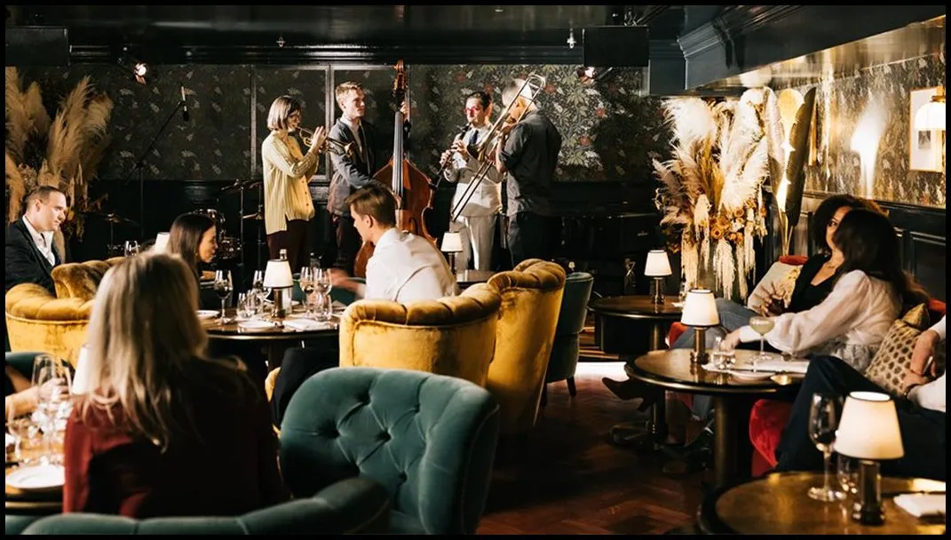A jazz band with trumpet, clarinet, trombone and double bass plays among velvet armchairs and lamplit tables at The Parlour