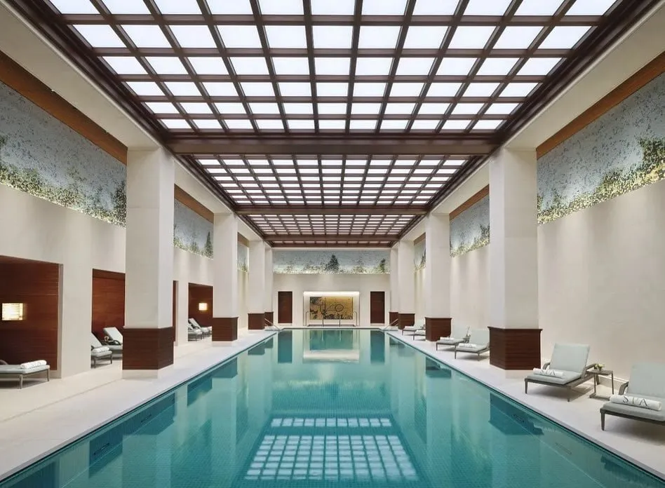 The underground pool at The Peninsula London, under a coffered ceiling of light panels, with mosaic landscapes on the walls