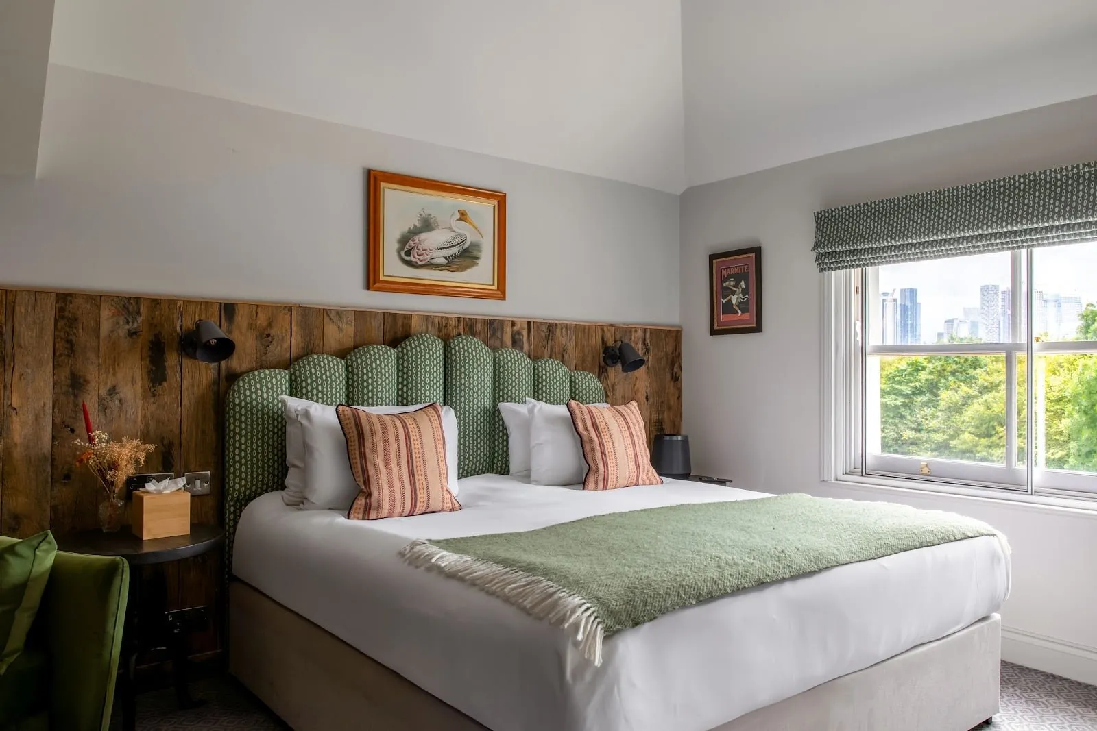 A double room at The Pilot with a green scalloped headboard, wood panelling and a window towards Canary Wharf