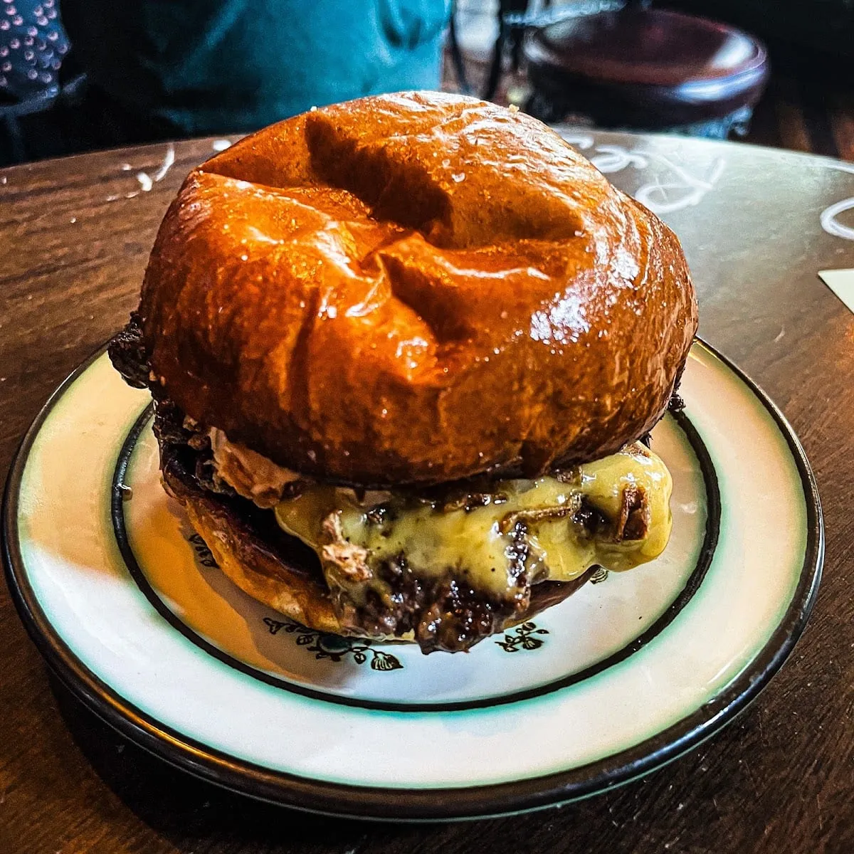 A cheeseburger with melted cheese on a glazed brioche bun, on a patterned plate at The Plimsoll