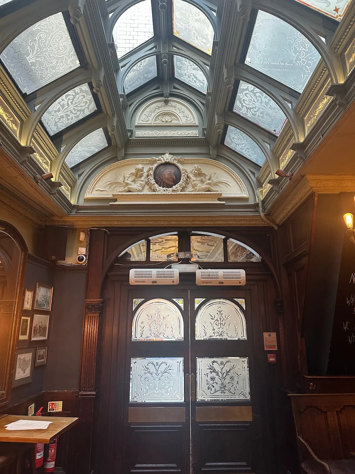 A glazed barrel-vaulted skylight above the entrance passage at The Punch Tavern, with an ornate plaster cherub medallion and etched glass doors below