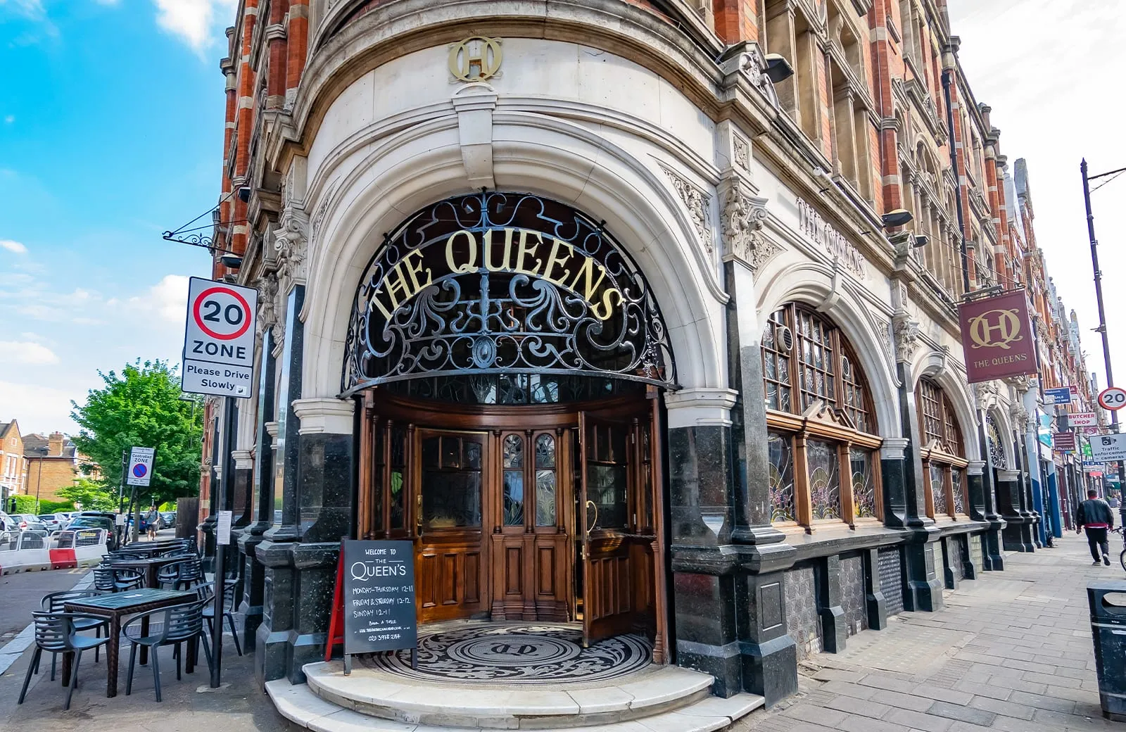 The Queens' arched entrance in Crouch End, with stained glass windows either side of the door and a round mosaic mat set into the threshold
