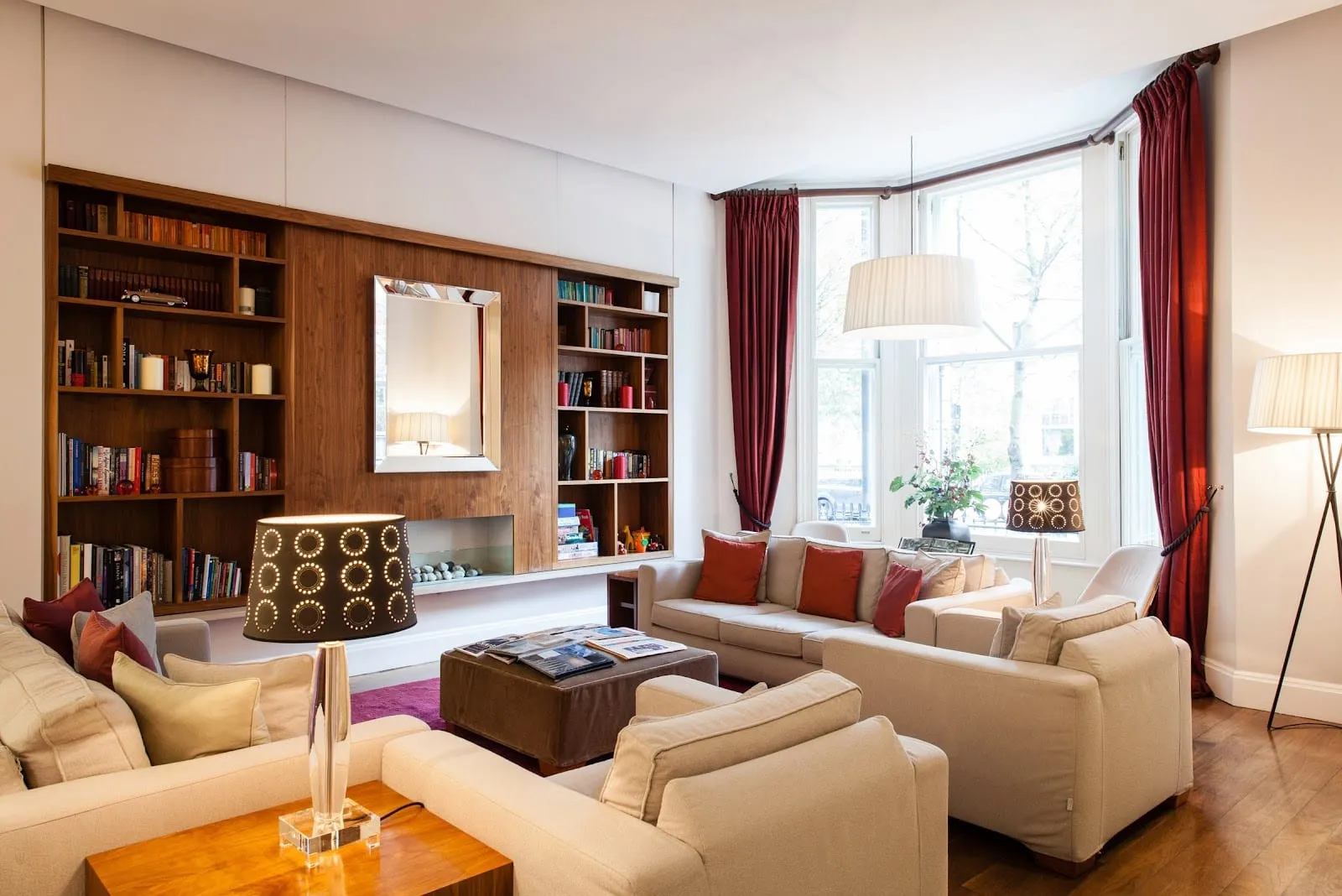 A lounge at The Rockwell with cream sofas, a low table, fitted bookshelves and a bay window