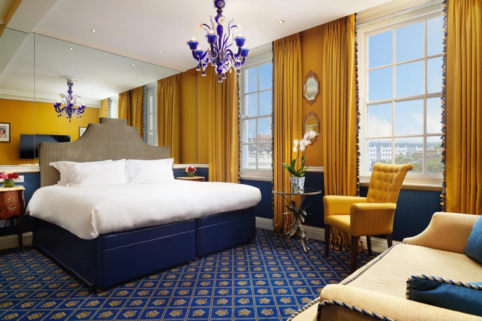 A bedroom at The Rubens at the Palace with a king bed, blue patterned carpet, gold drapery and views over the Royal Mews