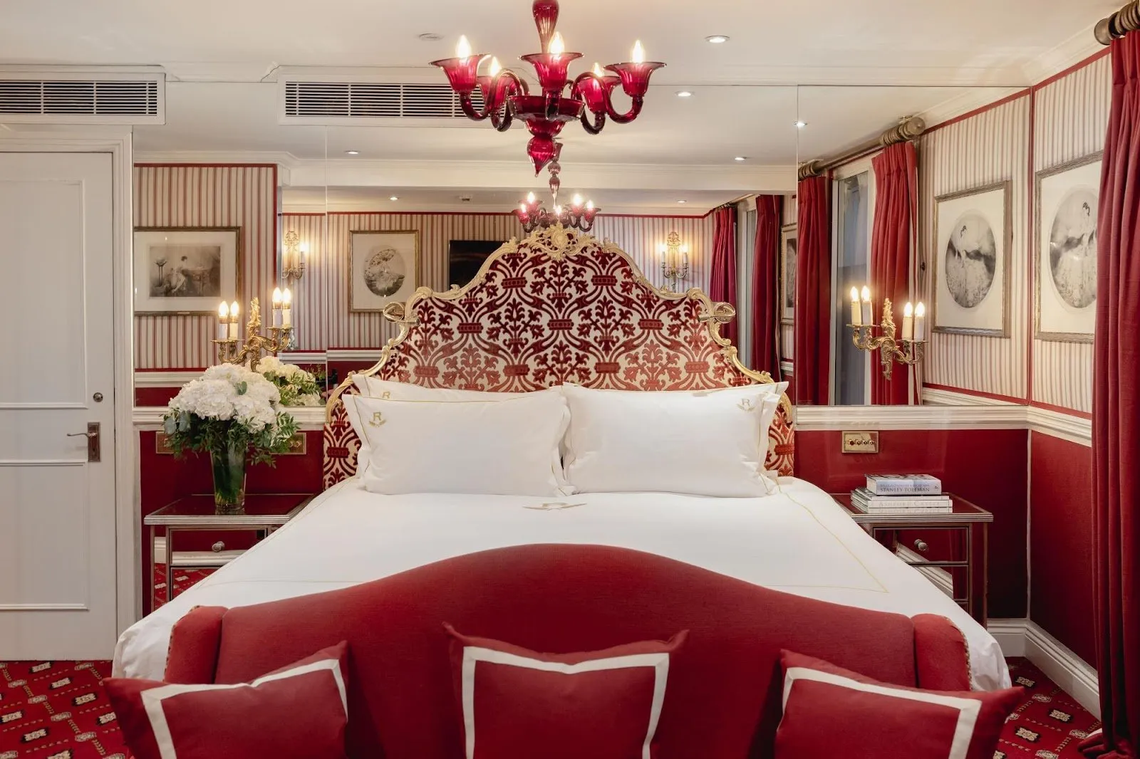 A red and gold suite at The Rubens at the Palace, with a damask headboard, ruby glass chandelier and monogrammed pillows