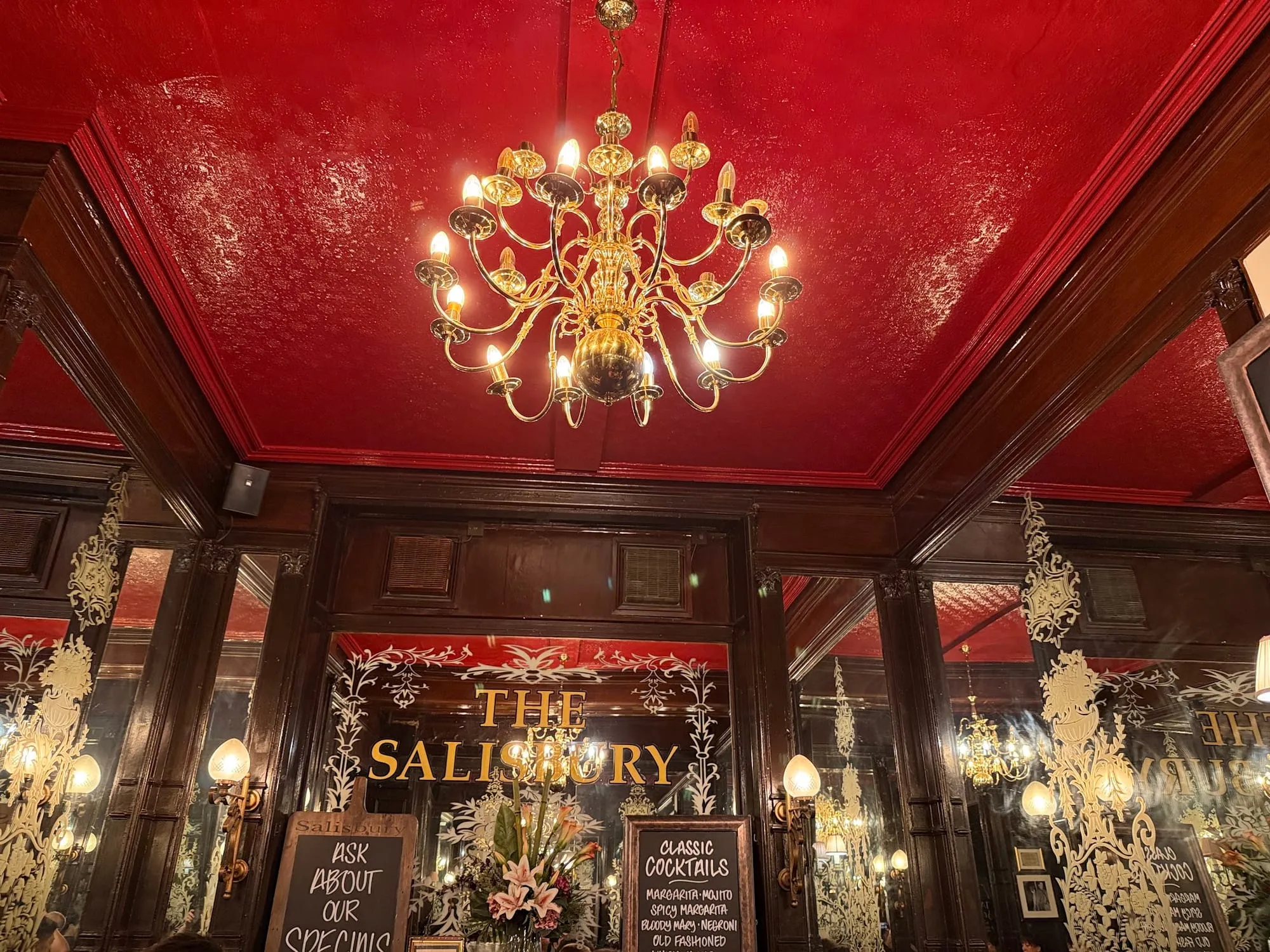 Etched glass mirrors and a gold chandelier inside The Salisbury on St Martin's Lane, with the pub's name lettered in gold across the mirror