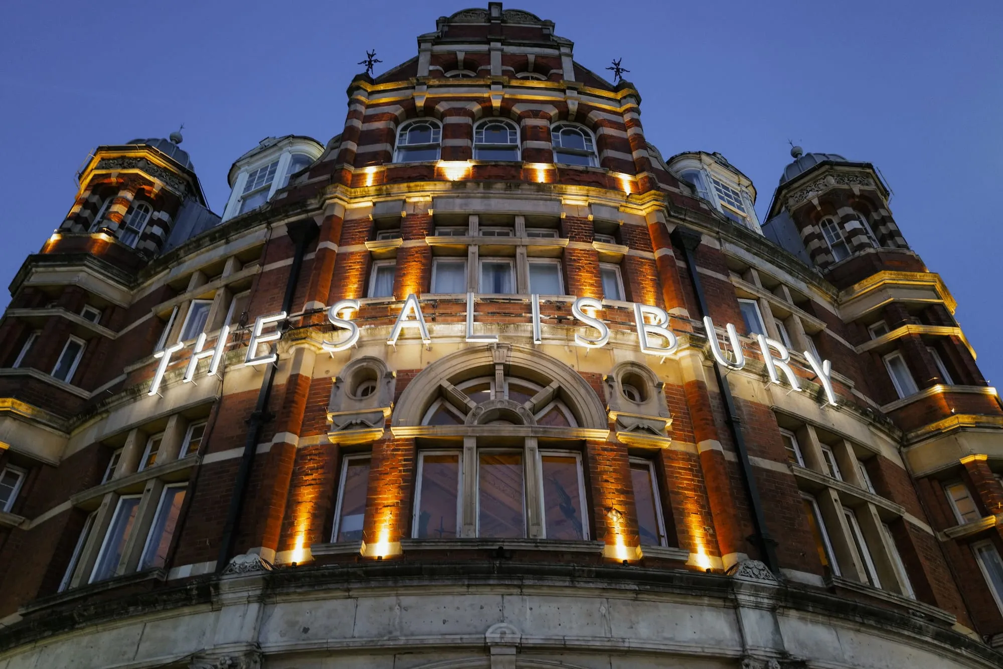 The Salisbury's ornate red-brick and terracotta corner tower on Green Lanes, Harringay, lit at dusk with its name spelled out across the facade