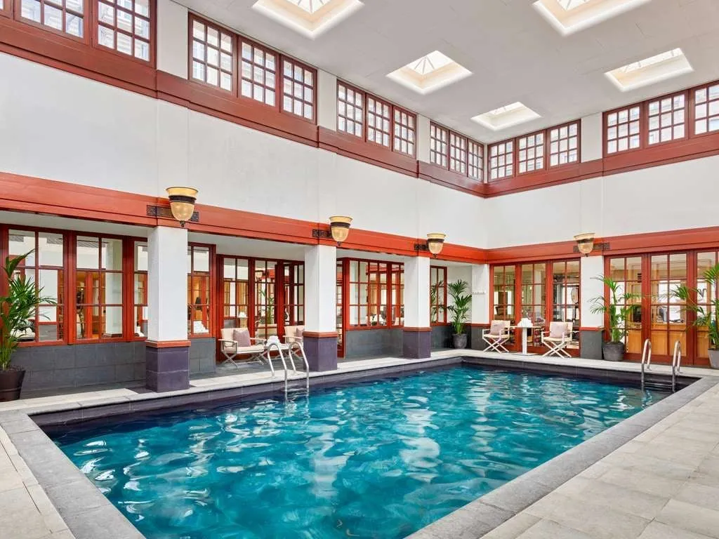 The atrium pool at The Savoy, ringed by white columns and red-framed windows under skylights