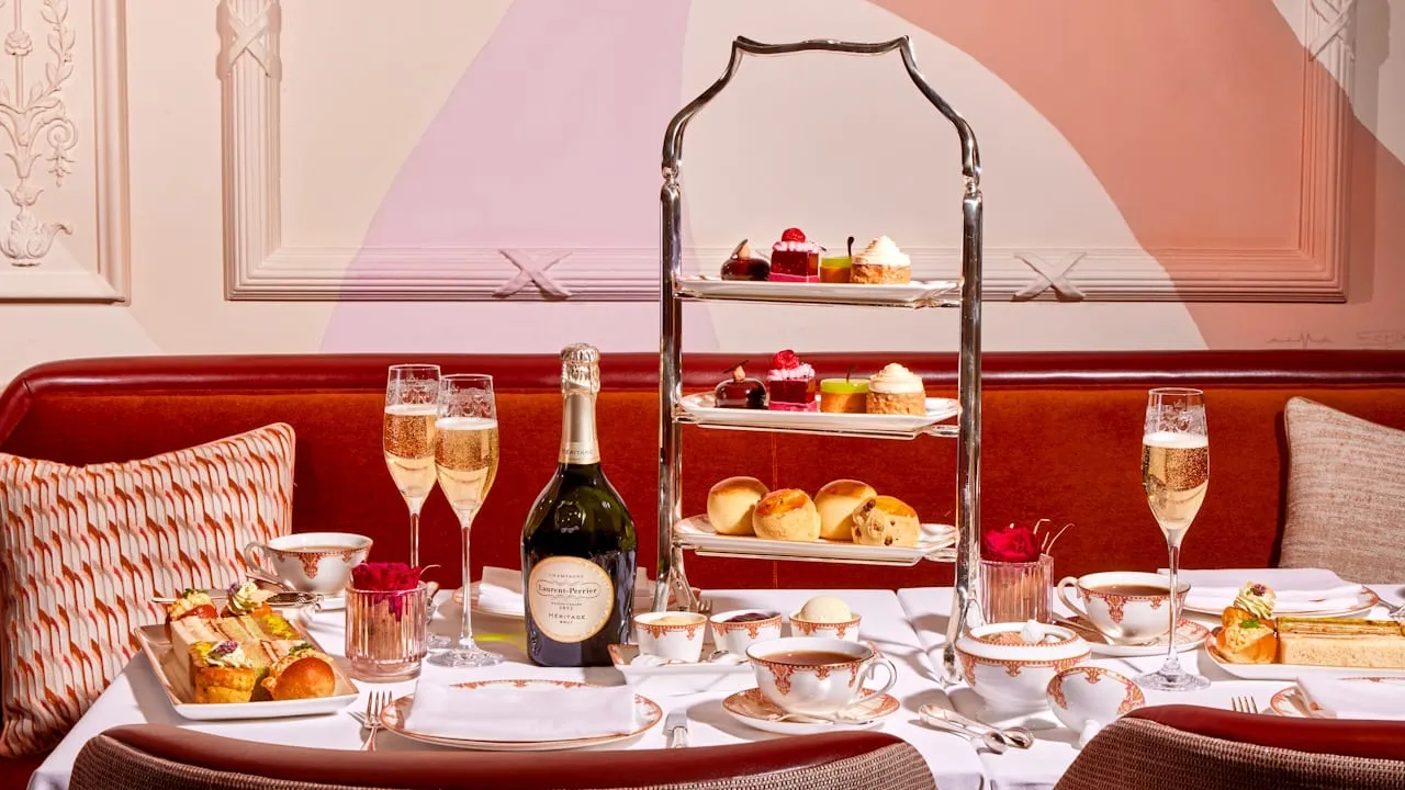 A tiered stand of scones and pastries on a white cloth against a red banquette, with champagne and ornate china