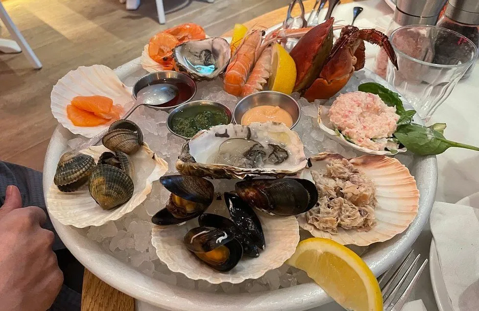 A round platter of ice holding oysters, mussels, clams, langoustines, a crab claw, smoked salmon and dressed crab, with three dipping sauces in the middle