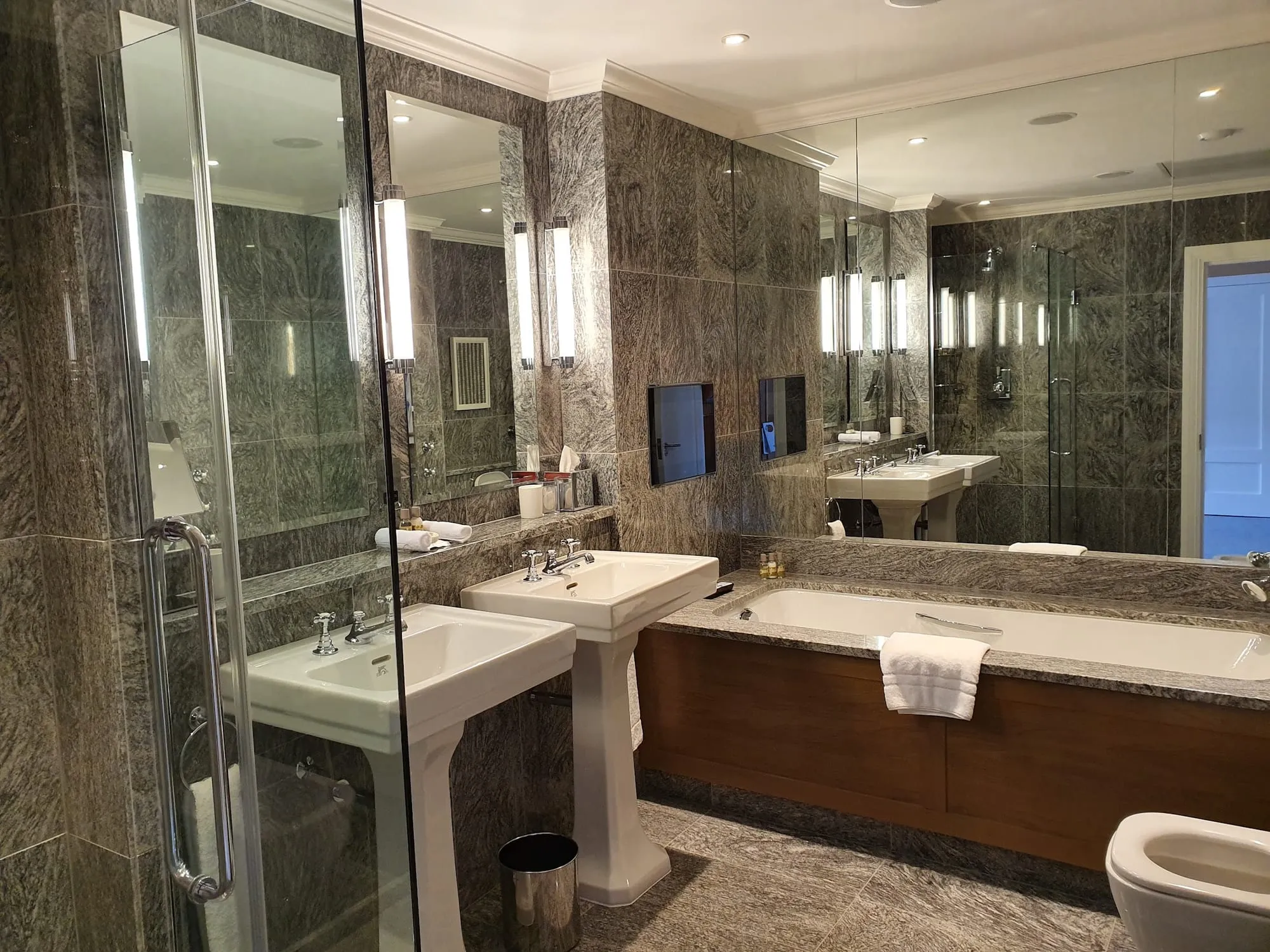 The bathroom at The Soho Hotel, with book-matched grey marble walls, twin pedestal sinks and a marble-surrounded bathtub