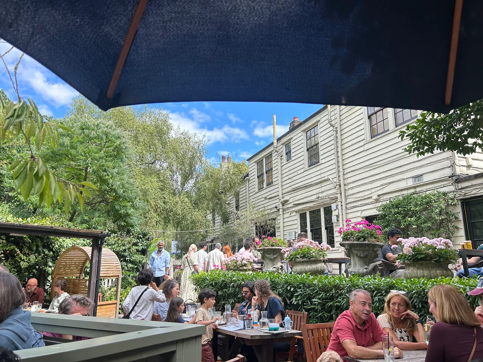 The busy garden at the Spaniards Inn in Hampstead, with stone flower urns and the white weatherboarded pub behind