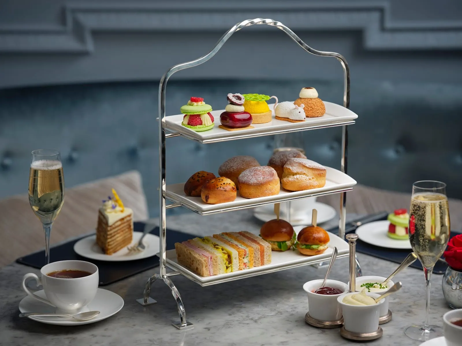 A tiered stand at The Stafford with savoury brioches, finger sandwiches, scones, and delicate pastries beside champagne flutes and a teacup
