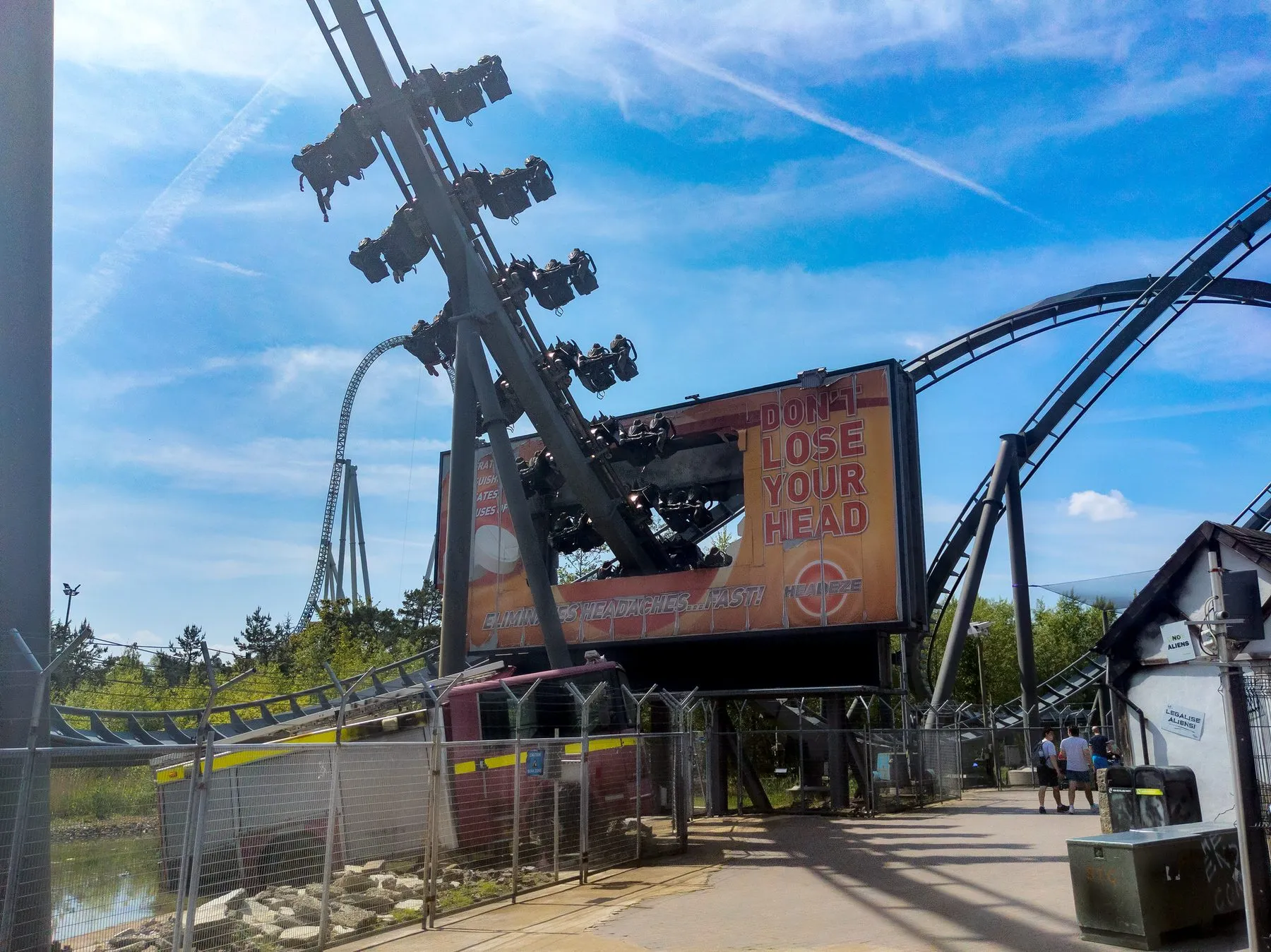 The Swarm at Thorpe Park, riders seated on the wings of the train as it passes a crashed advertising hoarding reading Don't Lose Your Head