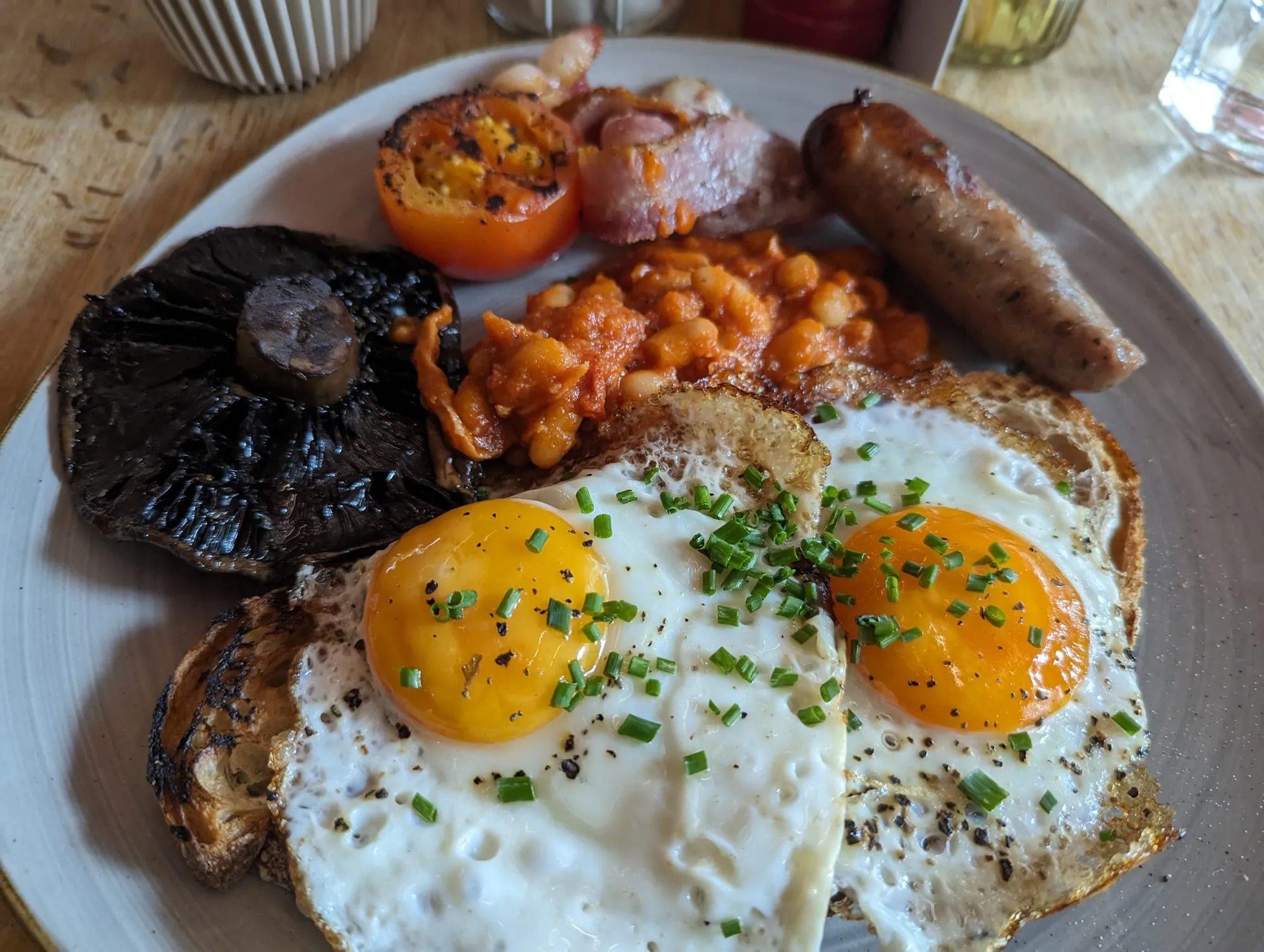 A full English breakfast of fried eggs, sausage, bacon, beans, grilled tomato and a field mushroom