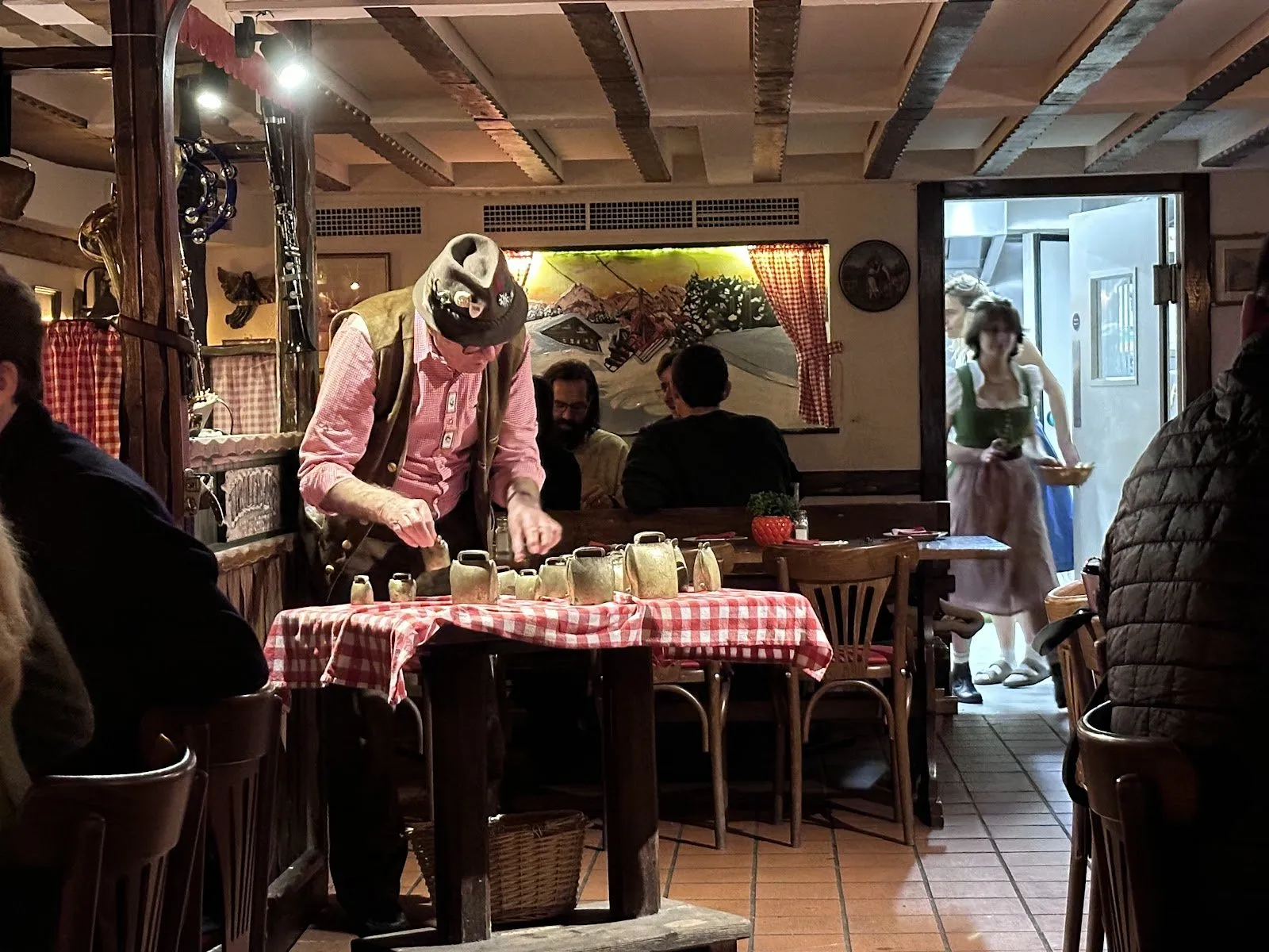 A man in Tyrolean dress lays out cowbells on a red-checked tablecloth for the show at The Tiroler Hut
