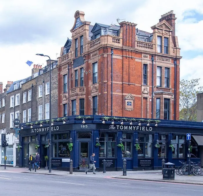 The Tommyfield, a red-brick corner pub on Kennington Lane with dark blue paintwork and hanging baskets