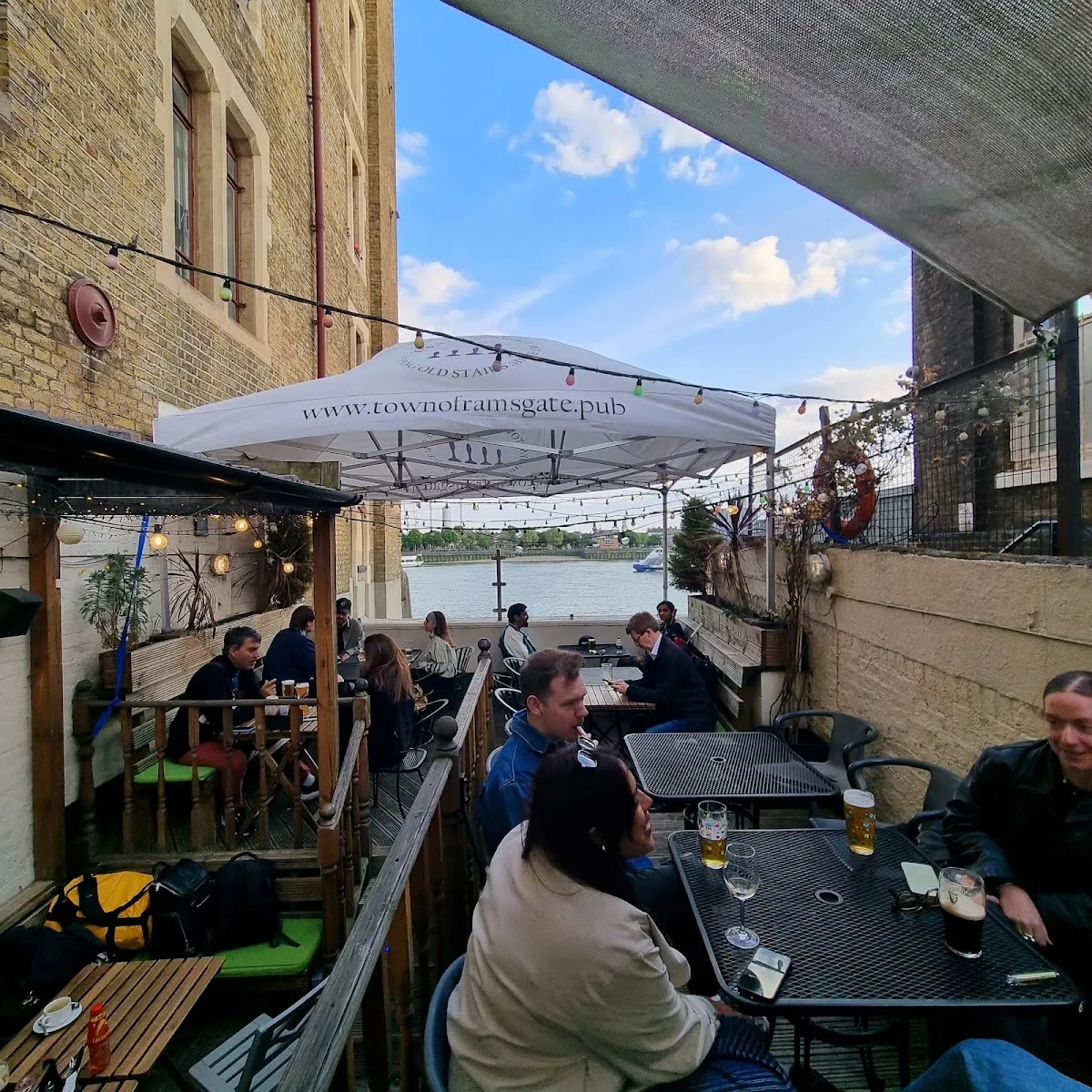 A handful of tables on the Town of Ramsgate's narrow river terrace at dusk, with the Thames beyond