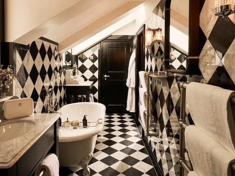 A Twenty Two bathroom under a sloping ceiling, with a claw-foot roll-top bath, black and white harlequin marble walls, a chequerboard floor and a heated towel rail