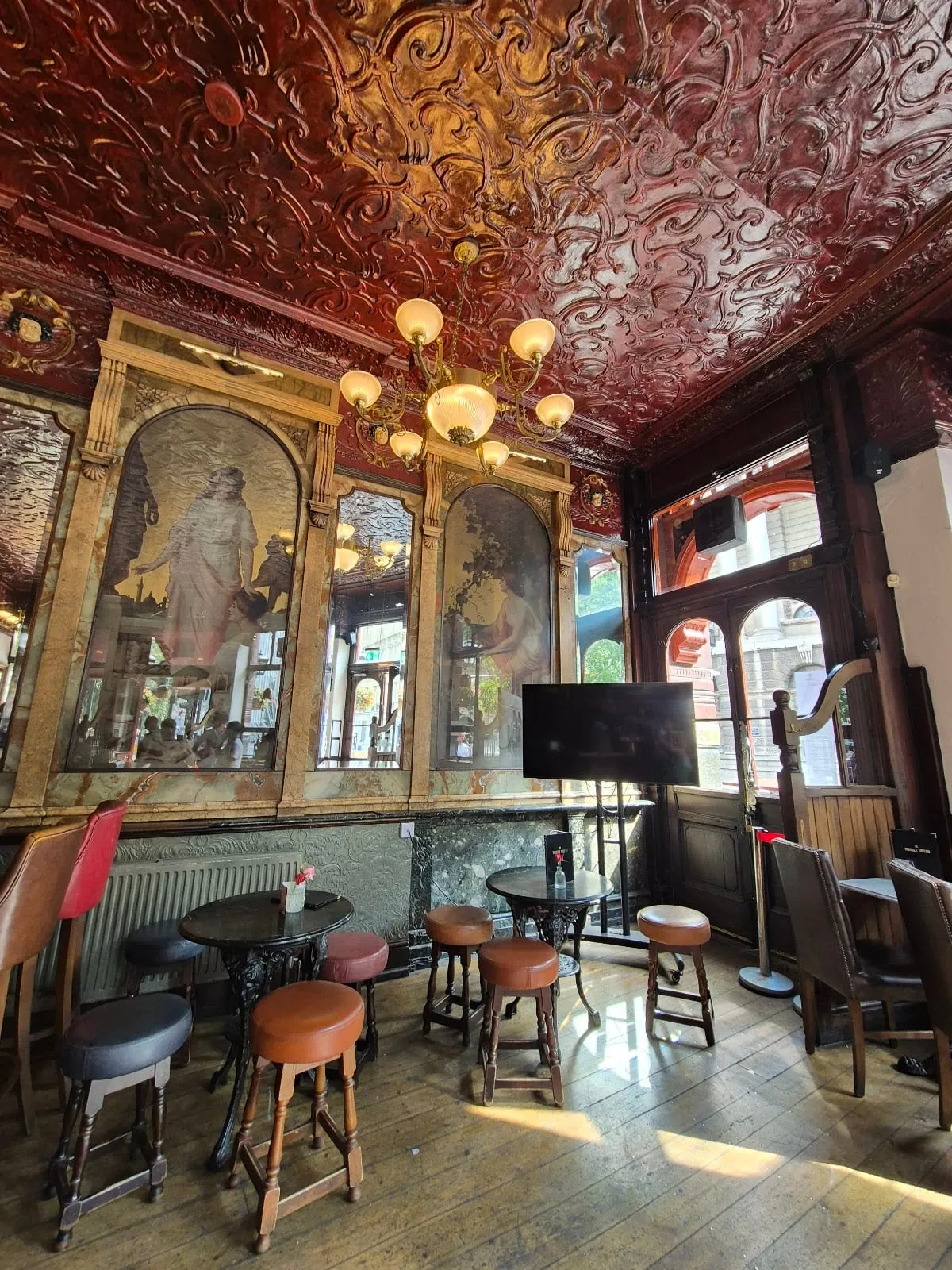 Arched gilt-framed panels alternating mirrors and paintings of classical women, under a deep red decorative ceiling inside The Viaduct Tavern