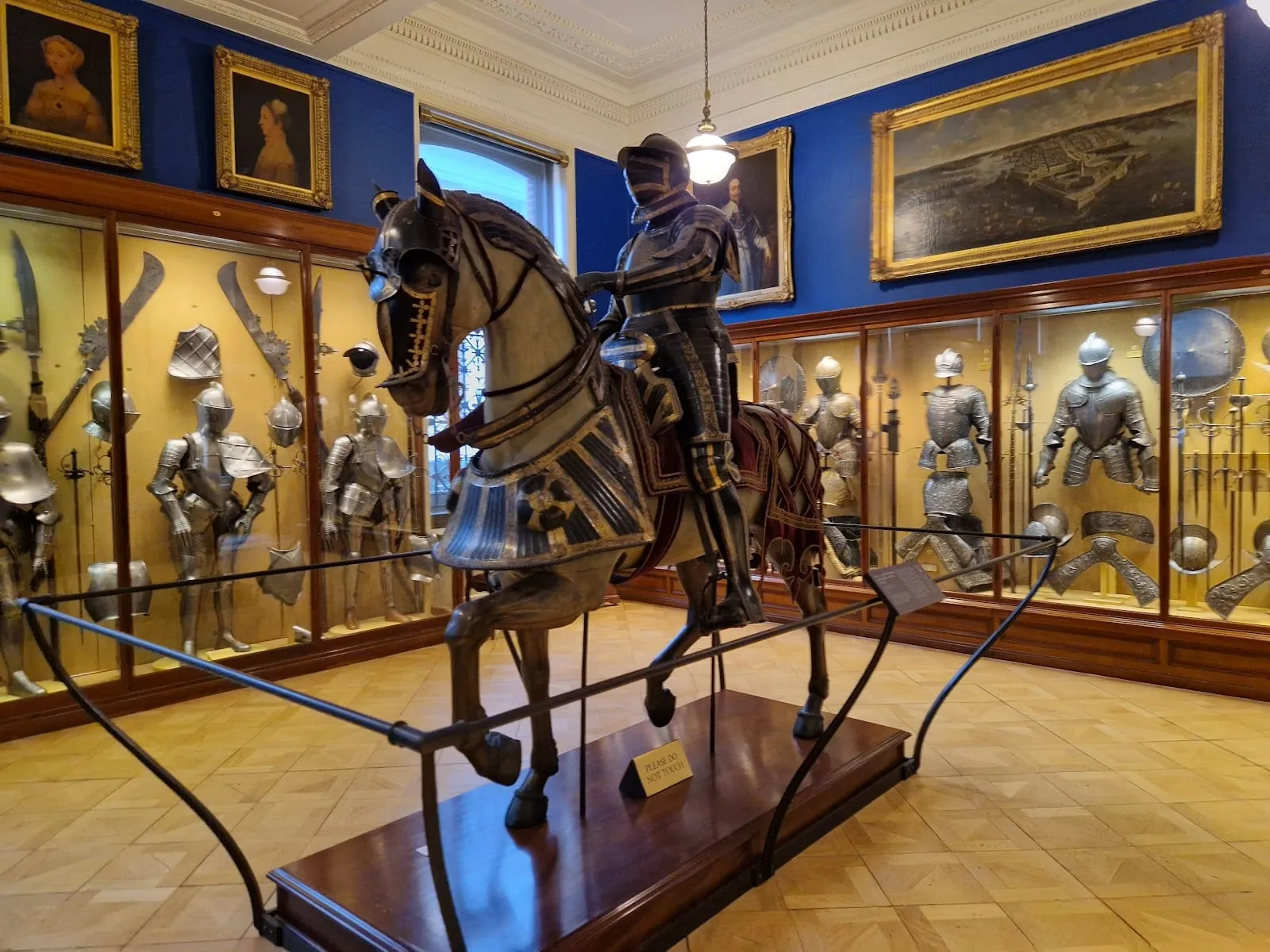 A suit of armour on a model of a horse and rider, surrounded by glass cases of swords, helmets and armour in the Wallace Collection's armoury