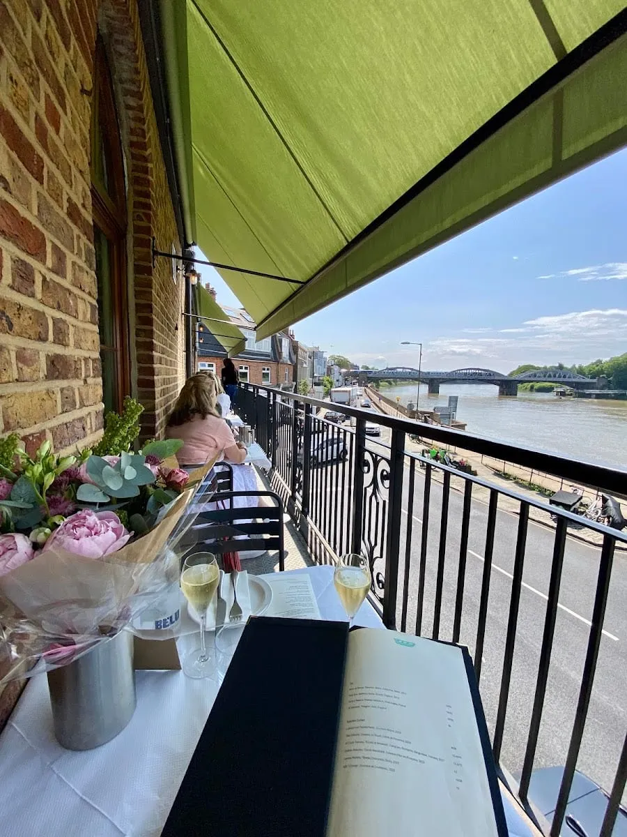The balcony at The Waterman's Arms overlooking the Thames and a railway bridge, with a table set with champagne glasses