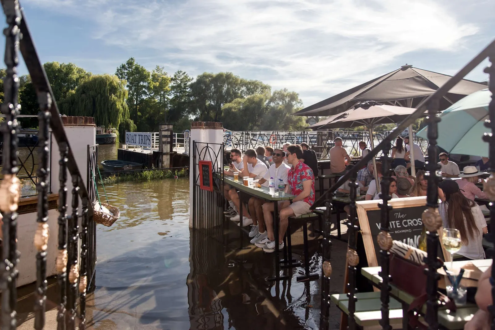 Drinkers at riverside tables outside the White Cross in Richmond, with the Thames lapping close to their feet