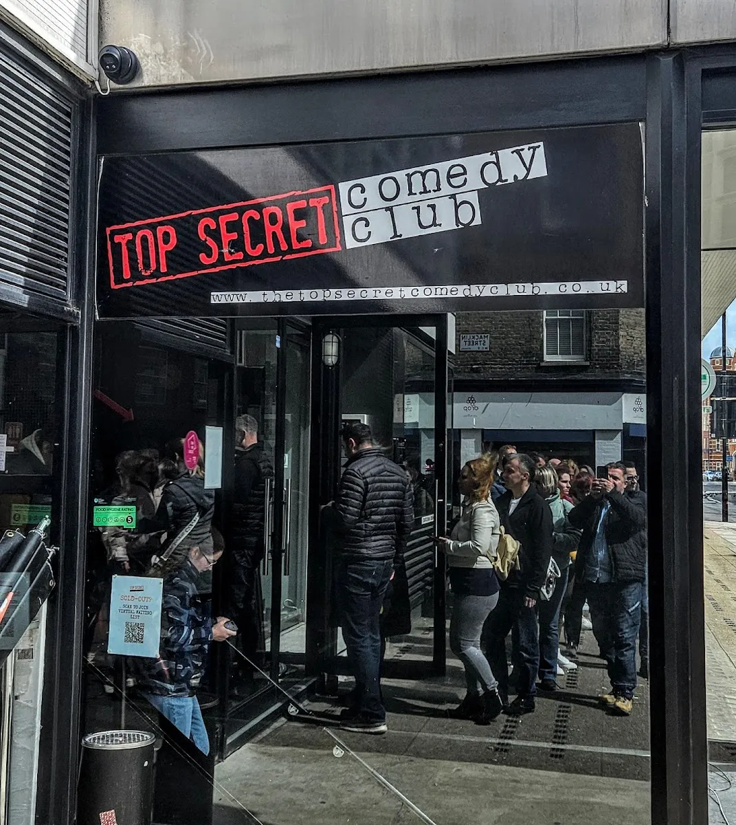 A queue of people outside the Top Secret Comedy Club entrance, with a "SOLD OUT" notice on the door