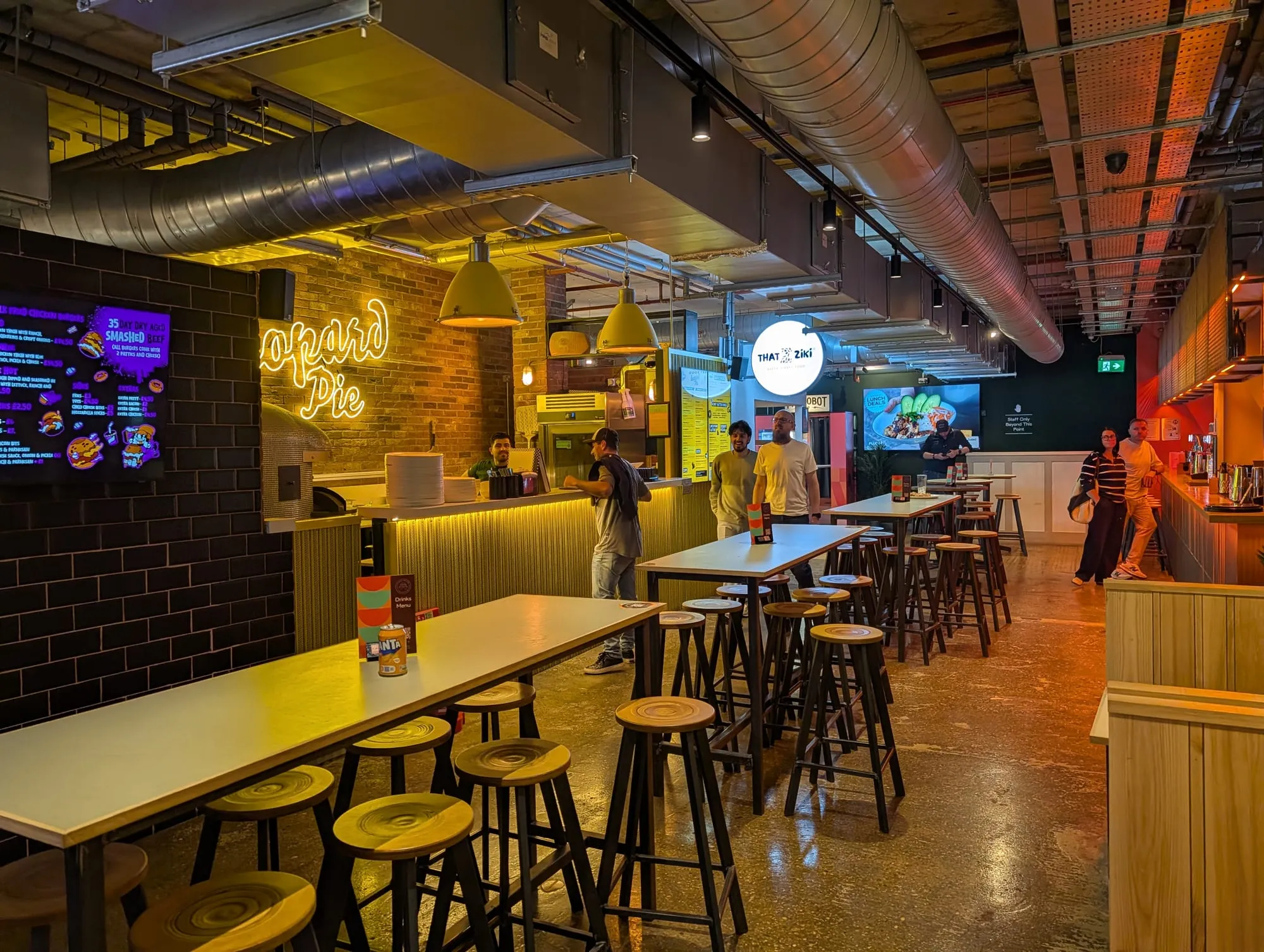 Long high tables under a neon sign inside the Tower Bridge Collective food hall