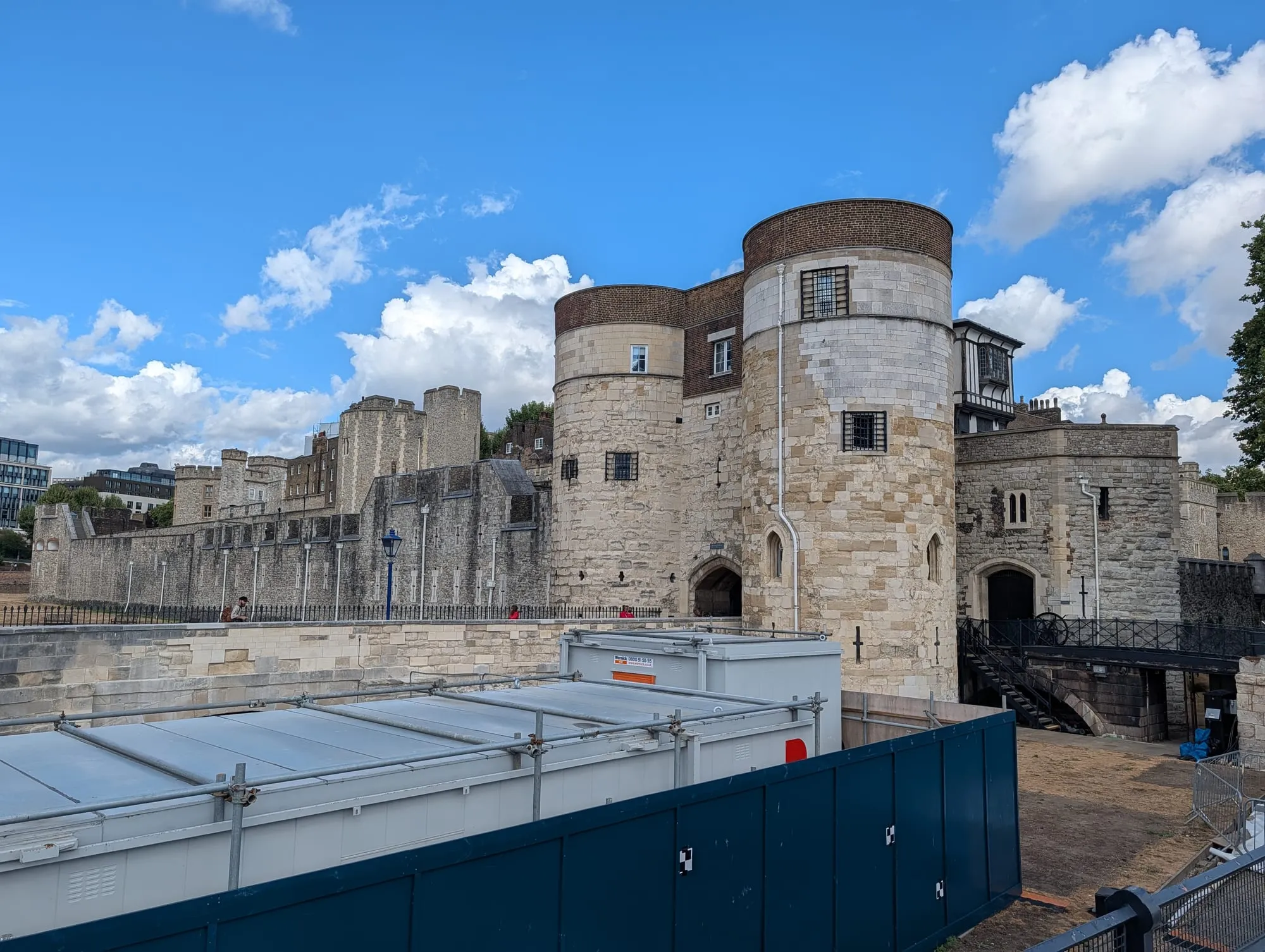 The Middle Tower and outer curtain wall of the Tower of London above the dry moat, with contractors' hoarding and site cabins along the near side